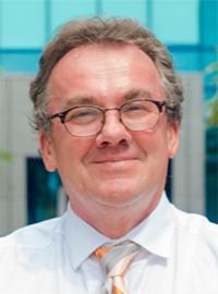 photo of man with short brown hair and glasses in white shirt and tie smiling outside