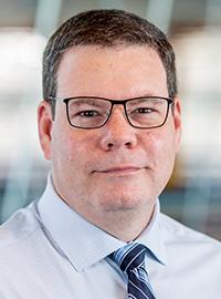 man in blue button-up shirt and blue striped tie and glasses looking at camera