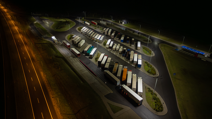 Aerial view of a truck stop at night, showcasing rows of parked semi-trucks illuminated by streetlights.