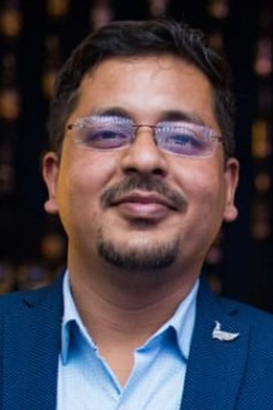man in blue suit and glasses with goatee looking at camera