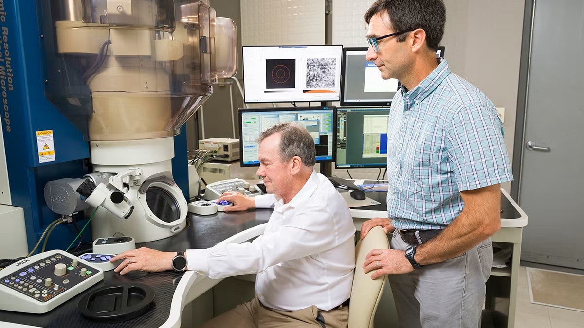 Professors pose with an electron microscope.