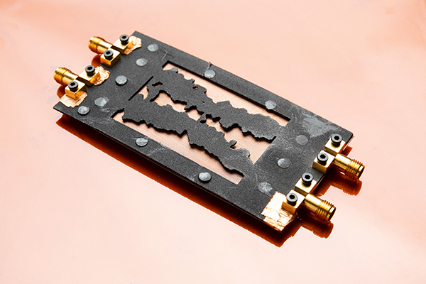 Close-up photograph of a rectangular electronic device with four gold-colored connectors on a copper-colored background.