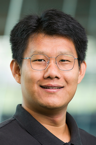 photo of man in glasses and black polo smiling at camera