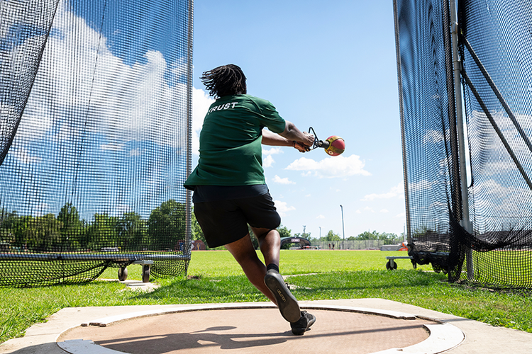 A strudent athlete completes a weight throw rotation inside an outdoor throwing cage