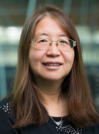 woman with long brown hair and glasses wearing black shirt smiling at camera