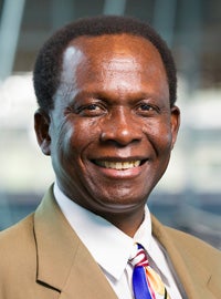 man with dark complexion and short hair in tan suit and white shirt colorful tie smiling at camera