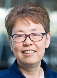 woman with short brown hair and glasses in blue collared shirt smiling at camera