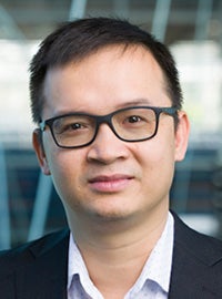 man with short black hair and black glasses smiling wearing white collared shirt and black jacket