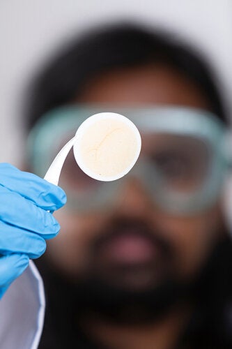 Close-up of a scientist holding a small circular filter disc with residue visible on its surface.