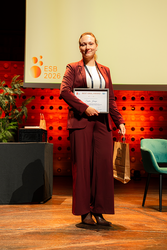 woman in maroon suit and white shirt standing holding frame certificate on stage