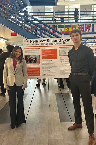 Two students stand on either side of their research poster, “PelliTect Second Skin,” by William Gragg and Andrea Ruiz, at a FAMU-FSU College of Engineering poster session. Other attendees and a row of international flags fill the atrium behind them.