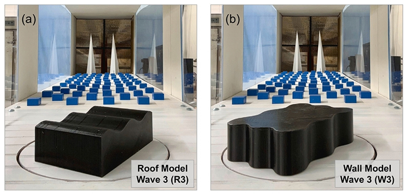 Two side-by-side photos of black building models inside a wind tunnel, with rows of small blue blocks and white cone-shaped spires behind them. Panel (a), labeled "Roof Model Wave 3 (R3)," shows a rectangular model with a wavy roofline. Panel (b), labeled "Wall Model Wave 3 (W3)," shows a model with wavy, curving sidewalls and a flat top.