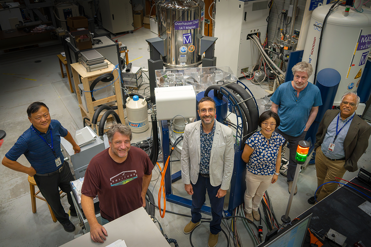 group of researchers standing in magent lab surrounded by equipment and looking at camera