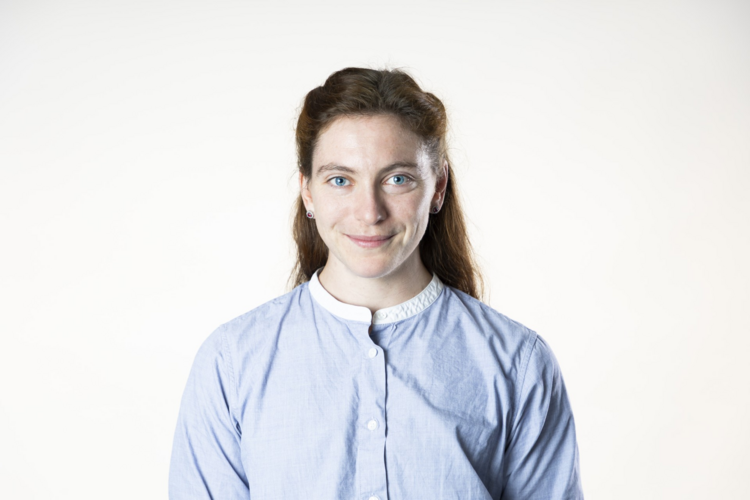 photo of woman with long dark hair smiling against white background wearing a white and blue button-up shirt