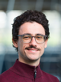 photo of man with dark hair mustache glasses in maroon zip up shirt