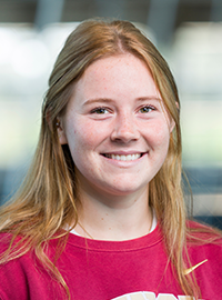 Portrait of a smiling young woman with long blonde hair wearing a red Seminoles sweatshirt against a softly blurred indoor background