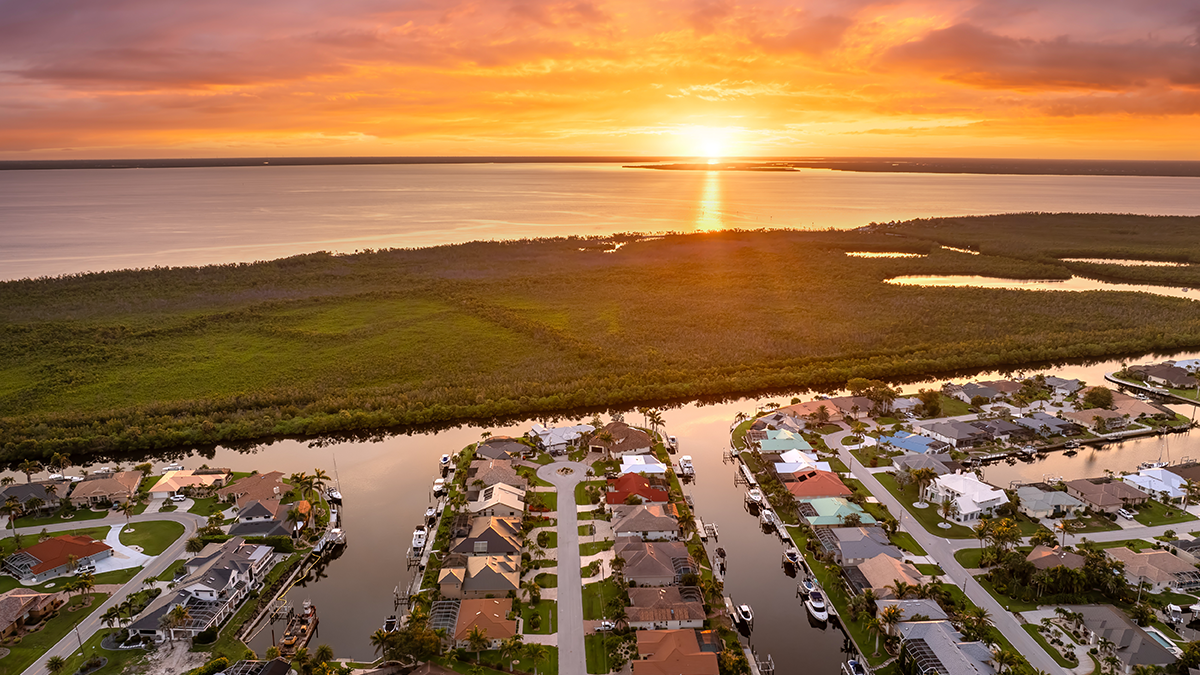 Sunset aerial view of Punta Gorda wealthy neighborhood. Expensive residential homes along canals reflect warm evening sky.