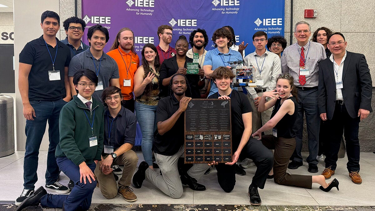 phot of a group of students with a trophy in front of an IEEE background