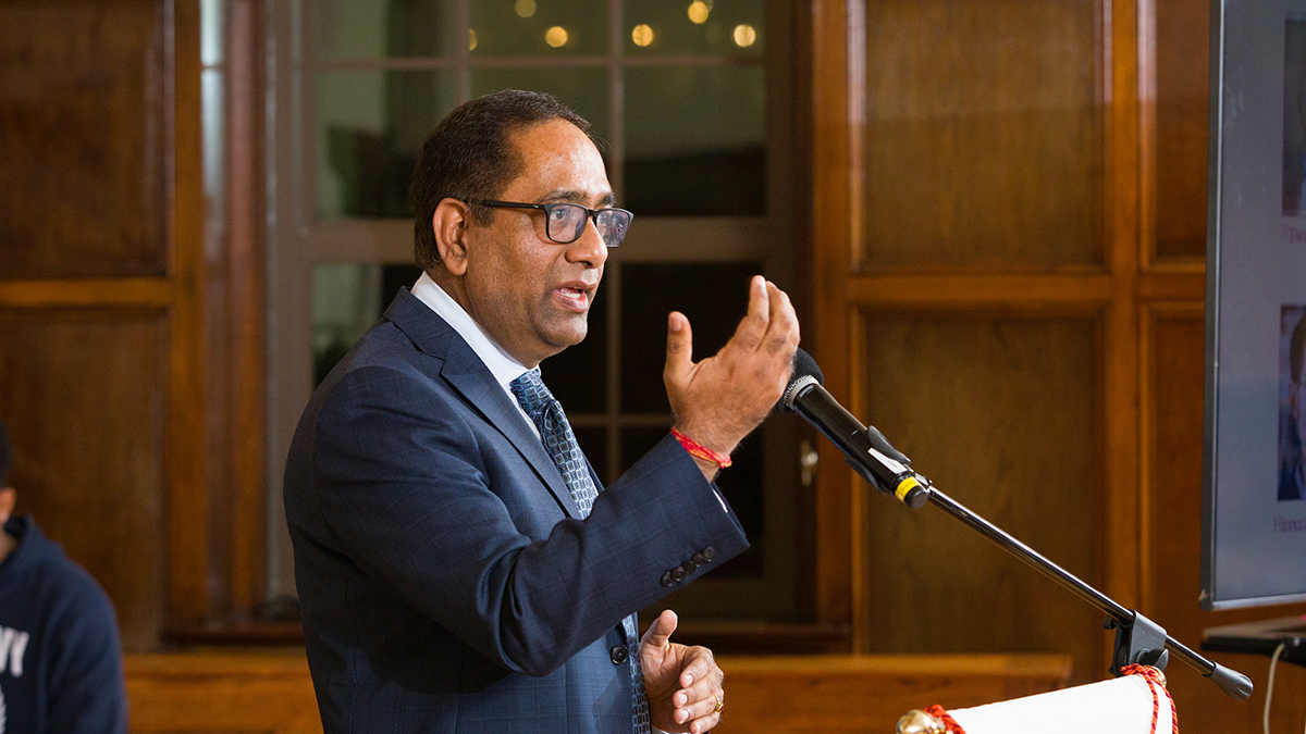 man in blue suit and black glasses talking at podium with hand guestures