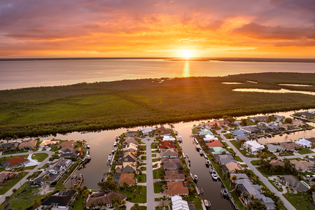 Sunset aerial view of Punta Gorda wealthy neighborhood. Expensive residential homes along canals reflect warm evening sky.