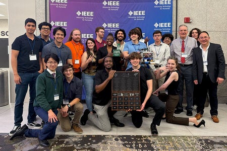 phot of a group of students with a trophy in front of an IEEE background