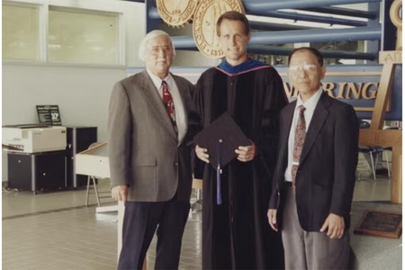 photo of two men and one graduate in robe standing together