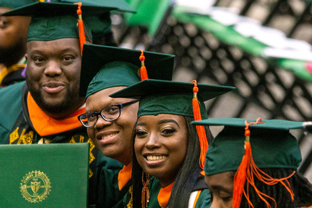 photo of students in green and orange cap and gown at graduation
