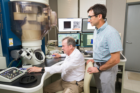 One researcher uses the controls of an atomic-resolution analytical microscope while another observes beside him.
