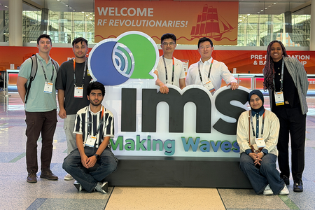 group of students stand behind and around a large logo of IMS making waves in text
