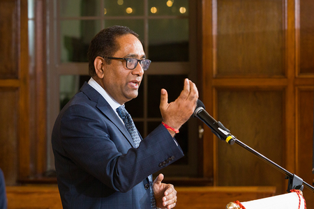man in blue suit and black glasses talking at podium with hand guestures