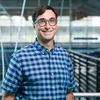 smiling man with short dark hair and glasses in blue plaid shirt