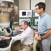 One researcher uses the controls of an atomic-resolution analytical microscope while another observes beside him.