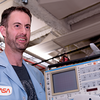 man in blue NASA shirt and beard smiling looking to right past camera
