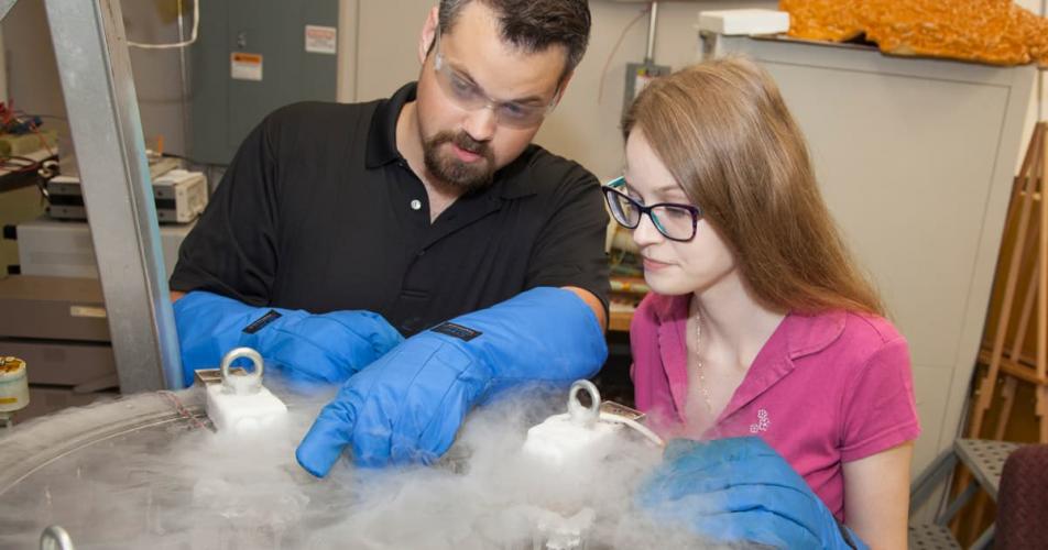 Two graduate students looking inside a cryo container.