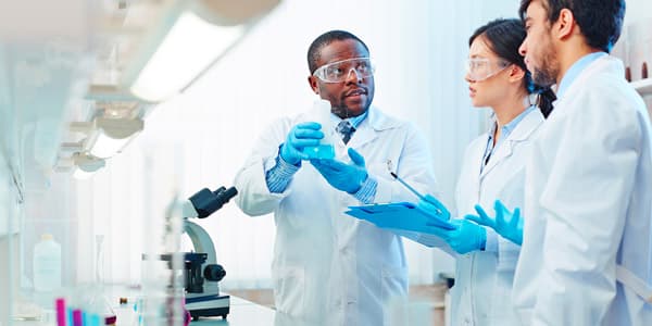 Professor displaying a compound in a beaker to two assistants