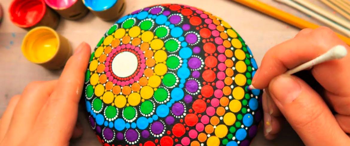 someone painting a mandala rounded rock