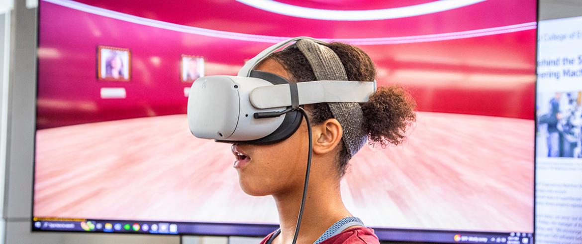 photo of teen girl wearing VR glasses in front of a large video display