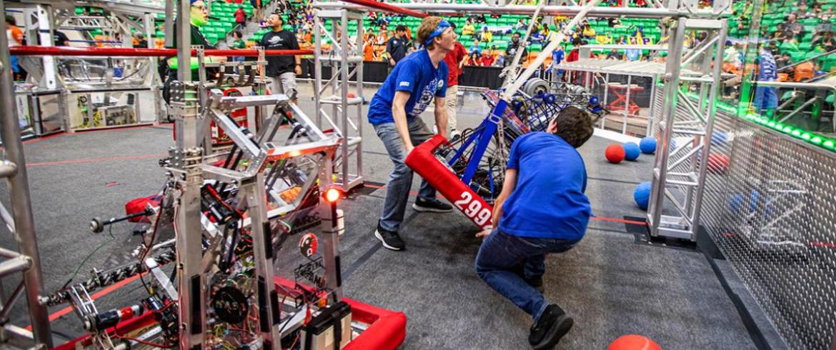 photo of two high school students carrying FRC robot on competition field