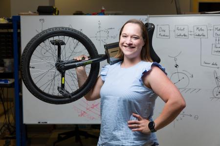 photo of taylor higgins phd with unicycle over her shoulder in front of math-filled white board at famu-fsu engineering